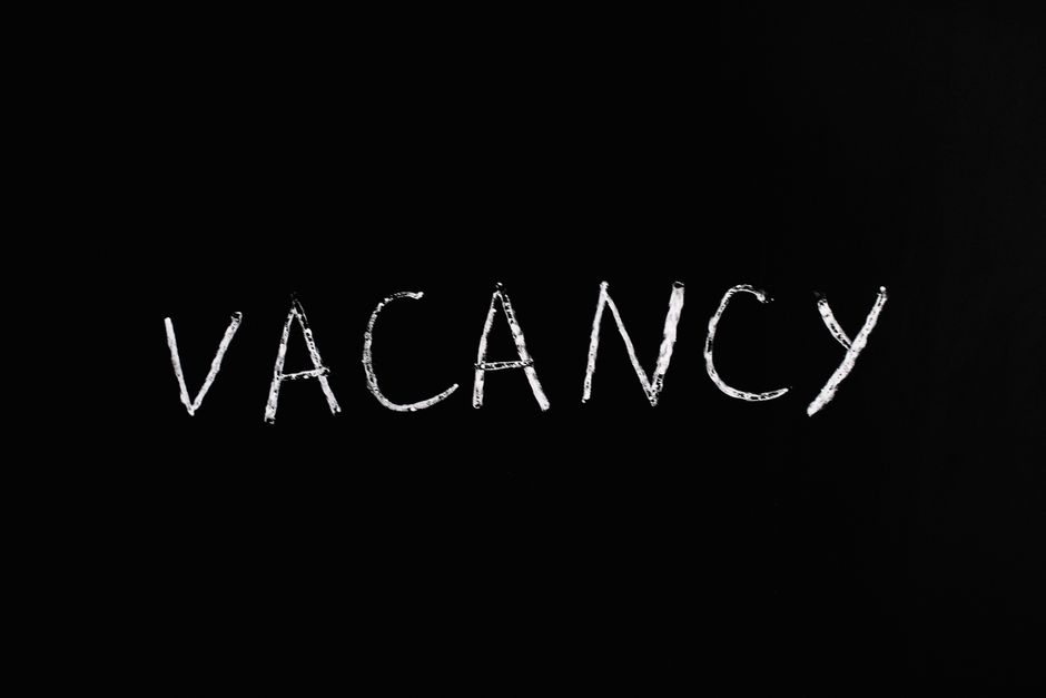 A black background with the word 'VACANCY' written in white chalk in the center, featuring a casual, handwritten style. The image highlights the concept of availability or open positions, which could 